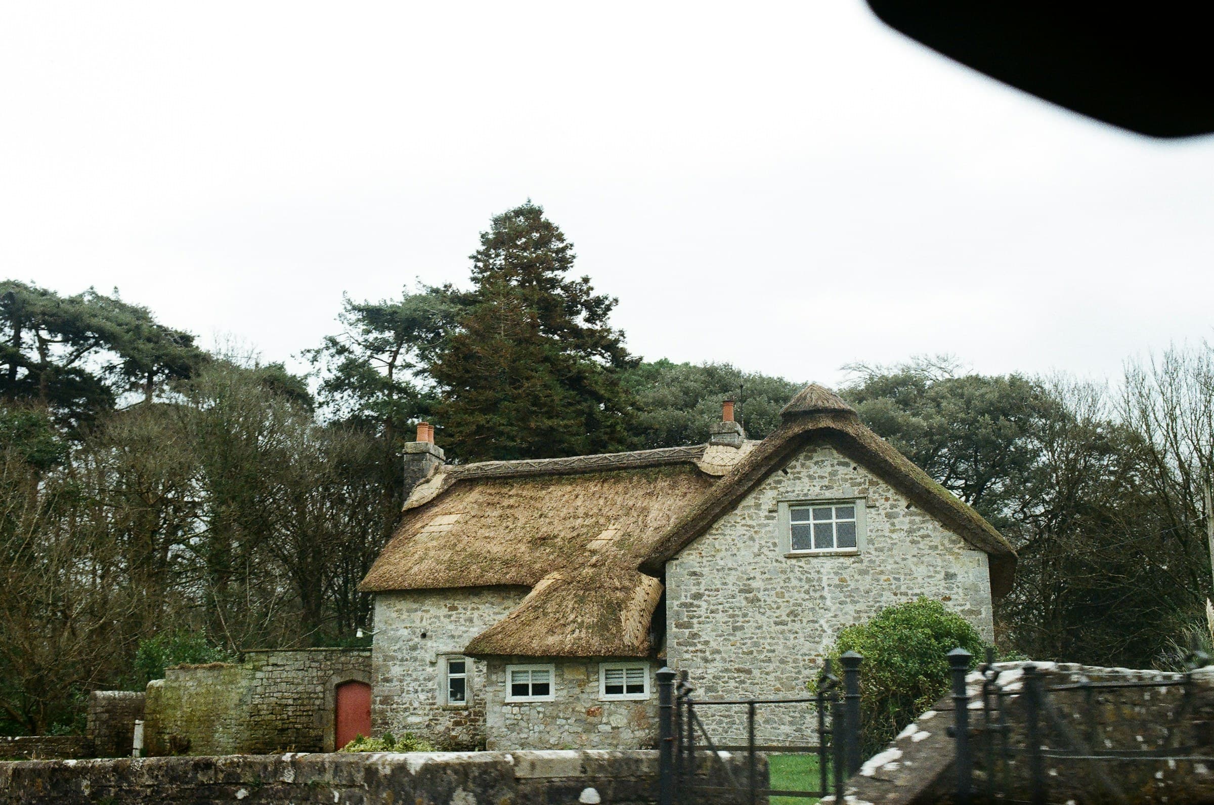 A stone-and-cob cottage with an oak-shingle roof, surrounded by mature trees and rebuilt from traditional materials after fire damage.