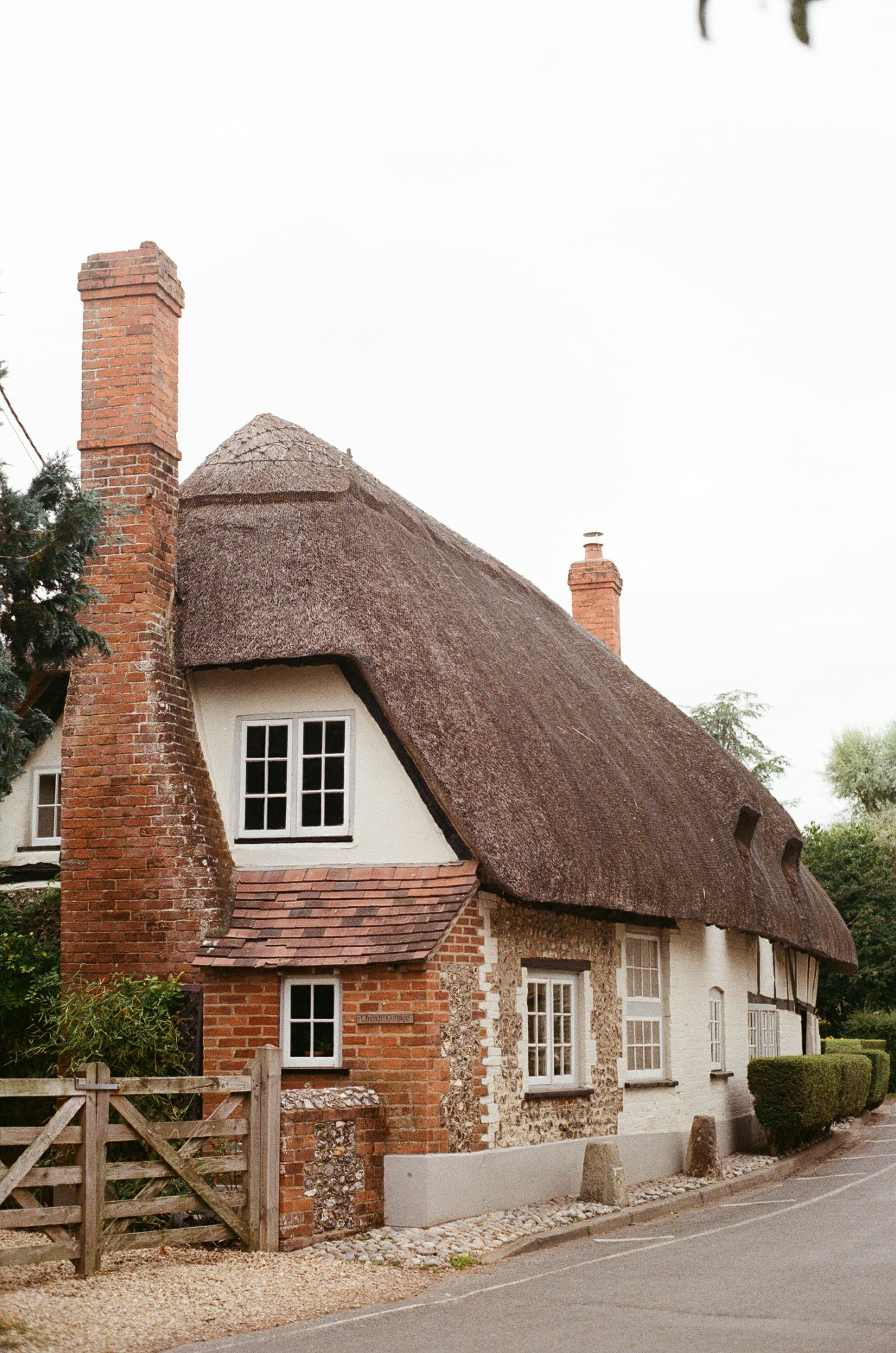 A charming sixteenth-century cottage with a long-straw thatched roof, lime-washed walls, brick chimney and a wooden garden gate.
