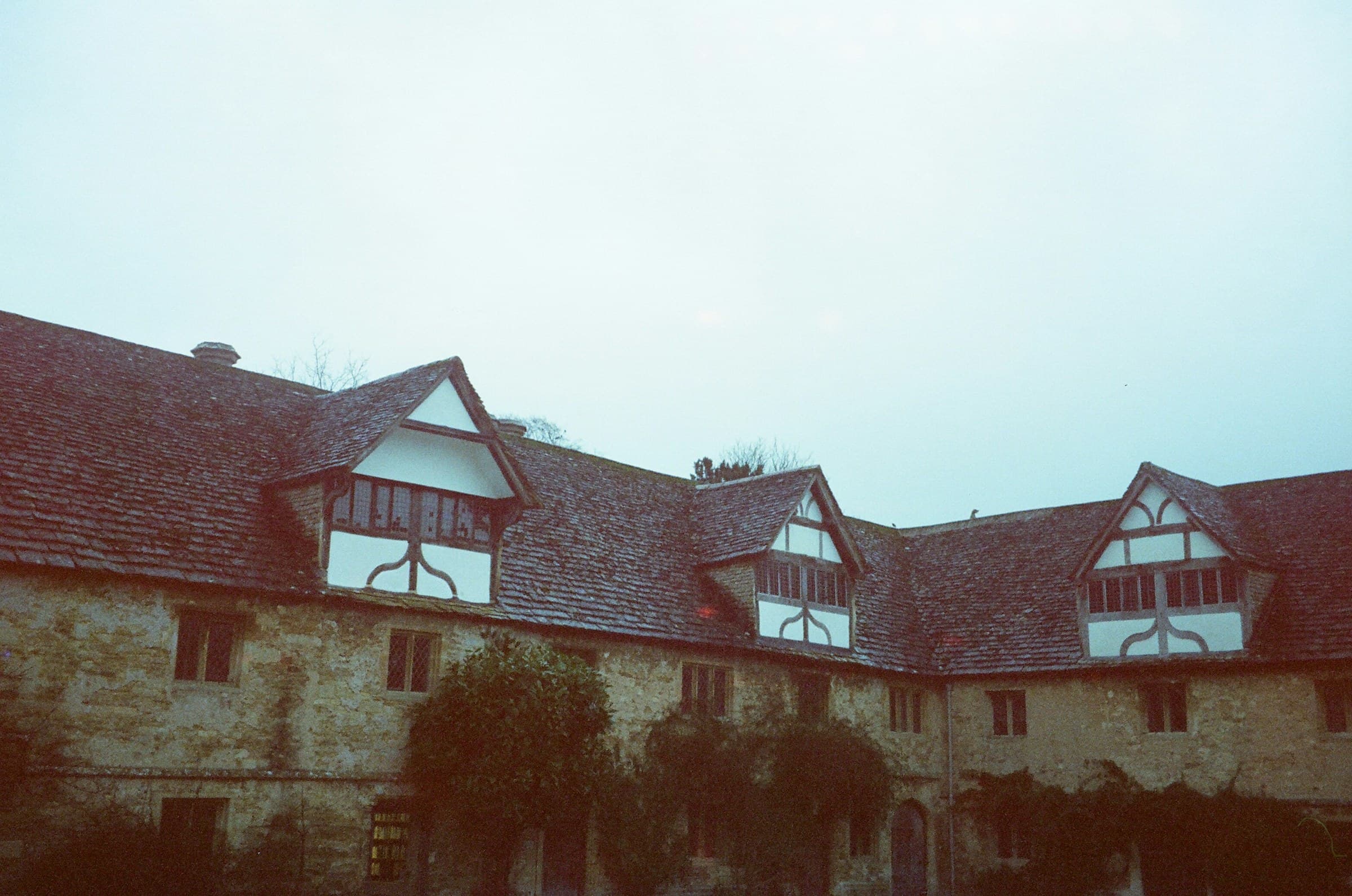 A Tudor-style building with exposed oak timber framing, lime-plaster infill and dormer windows in the pitched roof, photographed head-on in flat light.