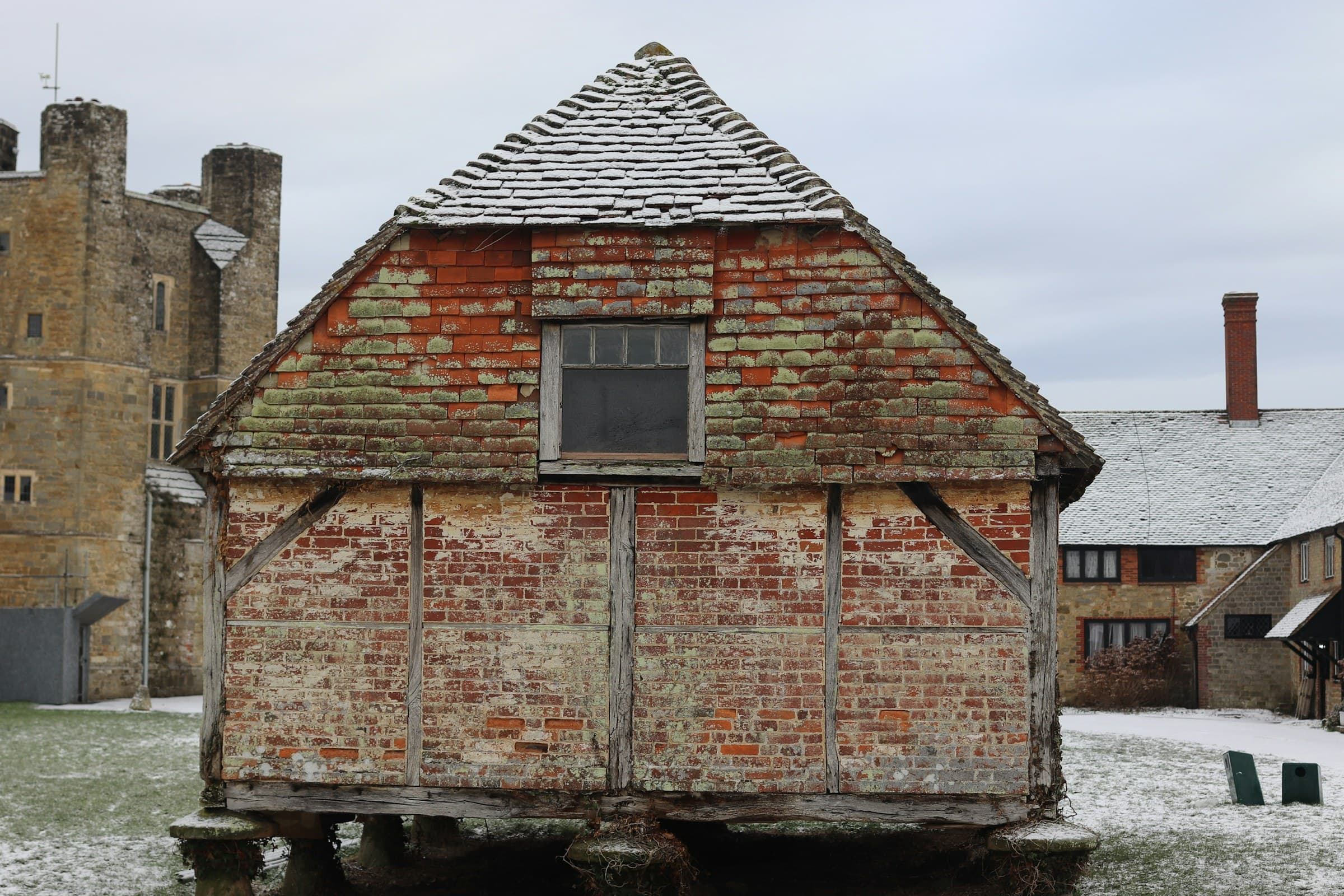 A weathered oak-framed threshing barn photographed in winter, its vertical board cladding and aged timber frame standing against a quiet sky.